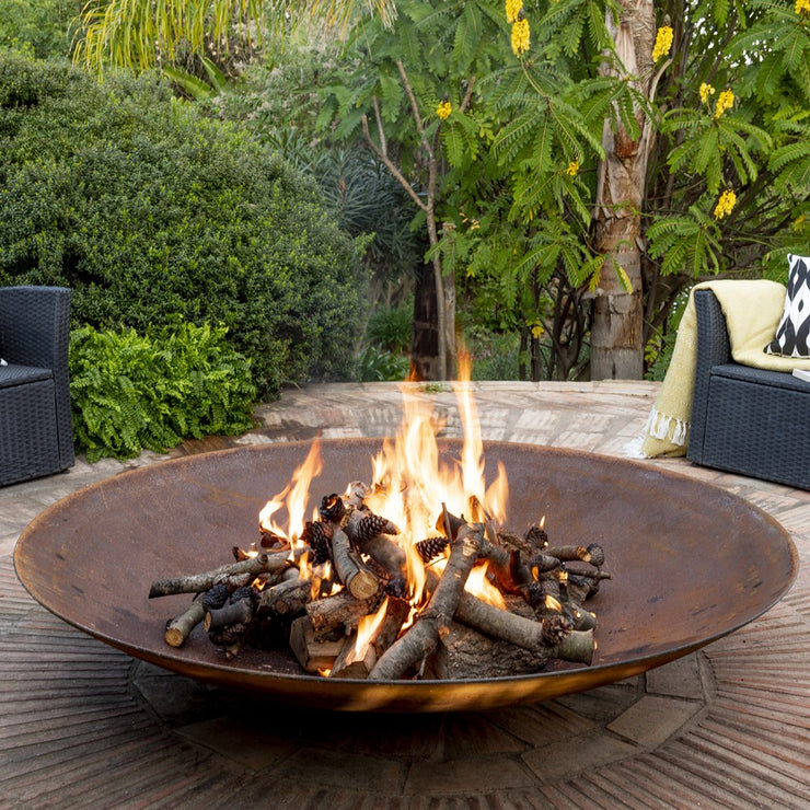 A large fire bowl burning with wood in a garden setting